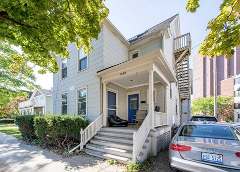 A silver car is parked in front of a two-story house.