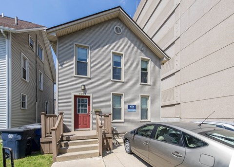 A silver car is parked in front of a two-story house with a red door.