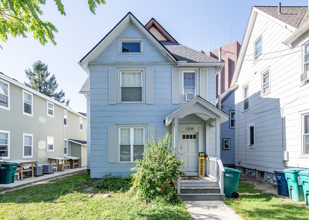 A blue house with a white door and windows is in front of other houses.
