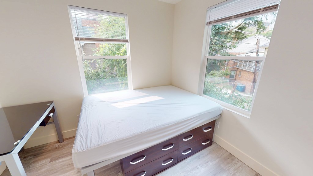 A white bed with a white mattress and a white pillow is in a room with a window.