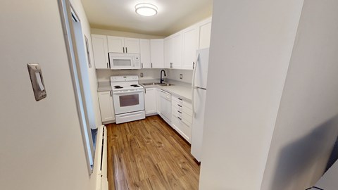 A kitchen with white cabinets and a wooden floor.