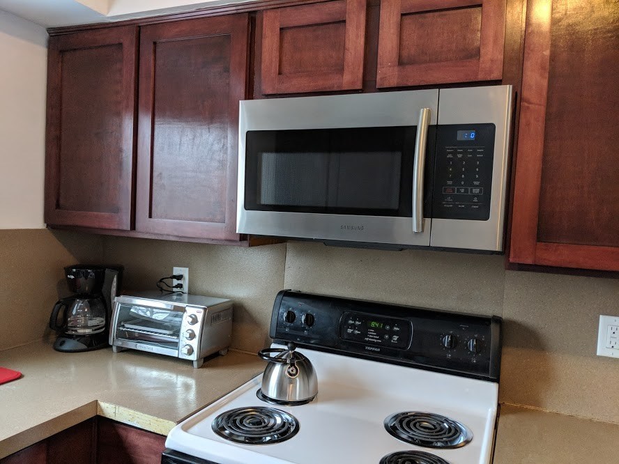 A kitchen with a white stove top oven and a silver microwave above it.