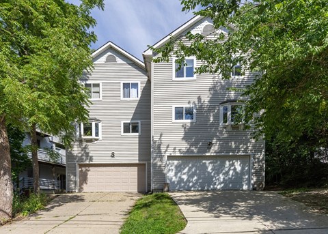 A two-story house with a garage is surrounded by trees.