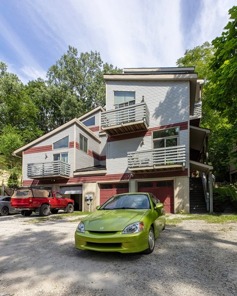A green car is parked in front of a two-story house.