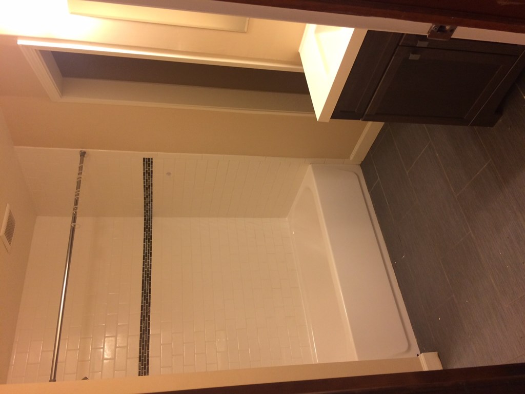 A shower with a white tiled wall and a silver shower head.