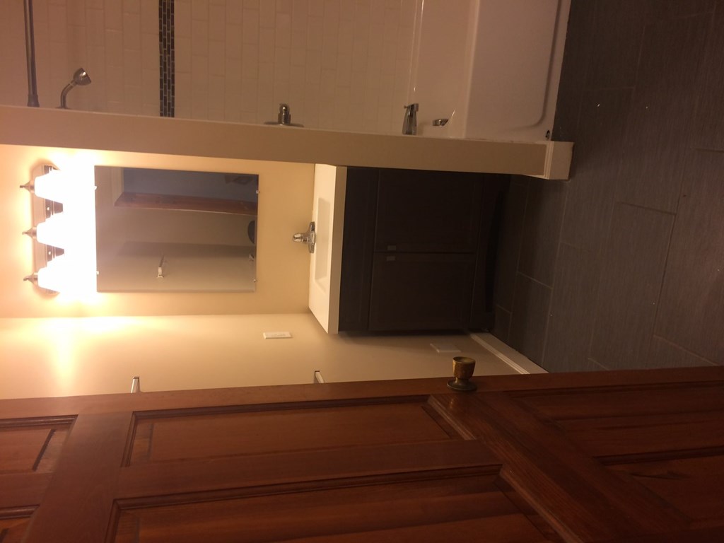 A wooden bench is in front of a mirror in a room.