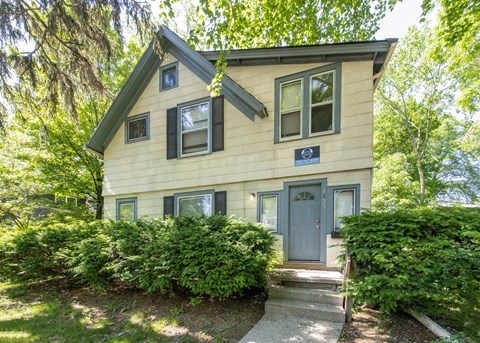 A small house with a grey door and windows surrounded by greenery.
