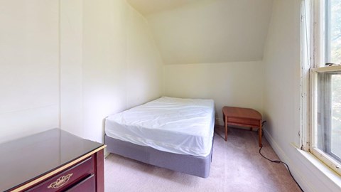A bedroom with a bed, a small table, and a window.