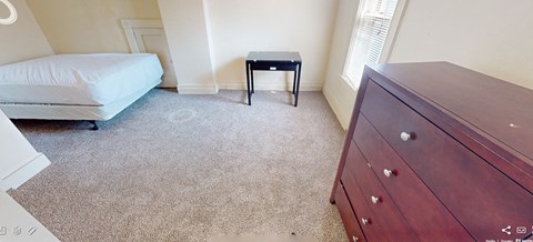 A bedroom with a bed, a small table, and a dresser.
