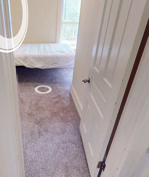 A white door is open to a room with a bed and a carpet.
