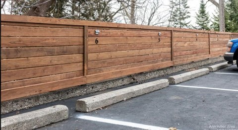 A wooden fence with numbered posts is next to a parking lot.