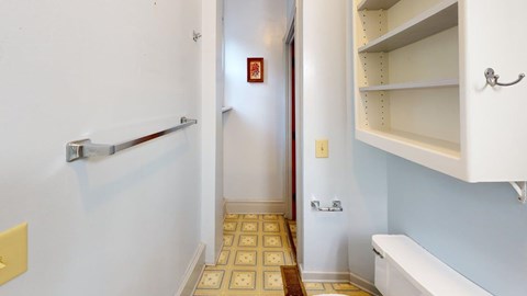 A hallway with a white wall and a tiled floor.