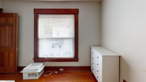 A room with a window, a white dresser, and a box on the floor.