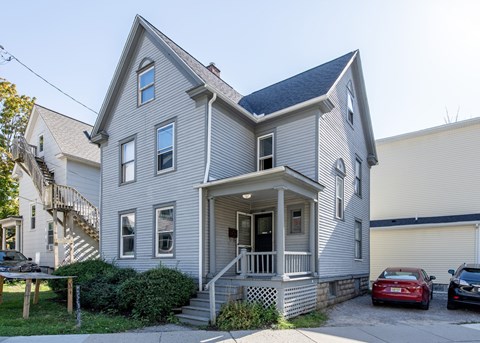A grey house with a red car parked in front.