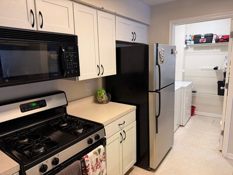 A black microwave and refrigerator in a kitchen with white cabinets.