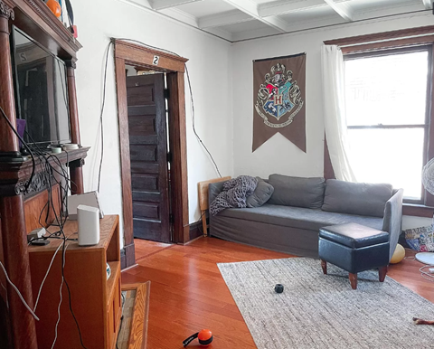 A living room with a grey couch and a Harry Potter banner on the wall.