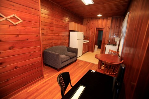 A small room with a couch, chair, table and a refrigerator.