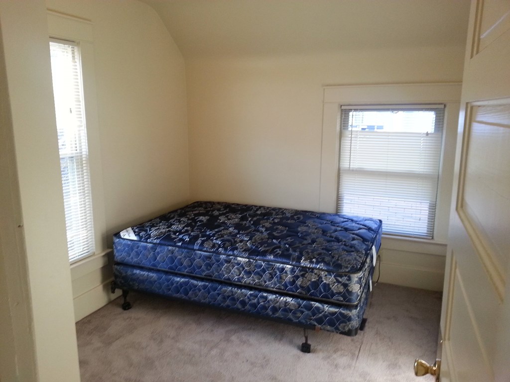 A blue mattress is on a bed frame in a room with a carpeted floor.