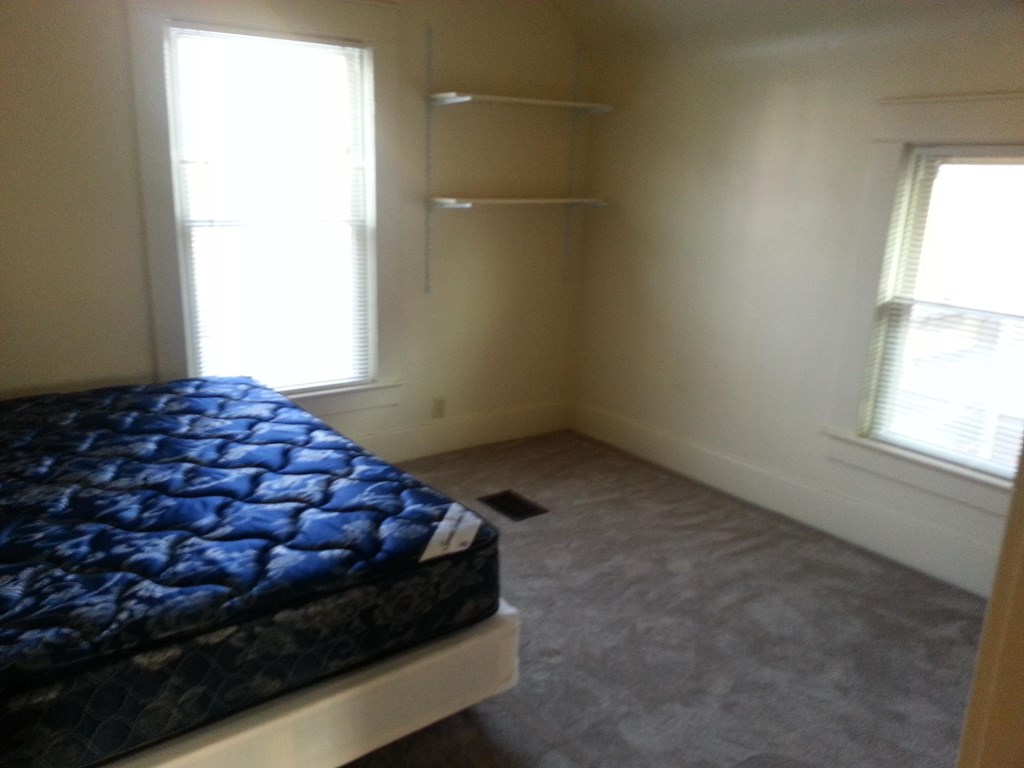 A bed with a blue patterned cover is in a room with a window.