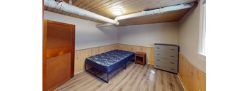 A bedroom with a bed, dresser, and a wooden door.