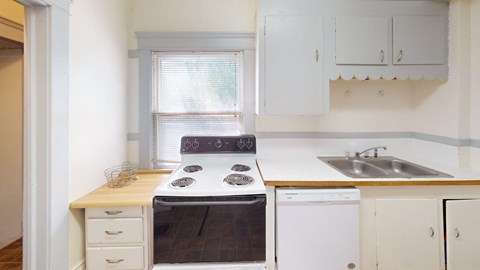 A white kitchen with a stove, sink, and cabinets.