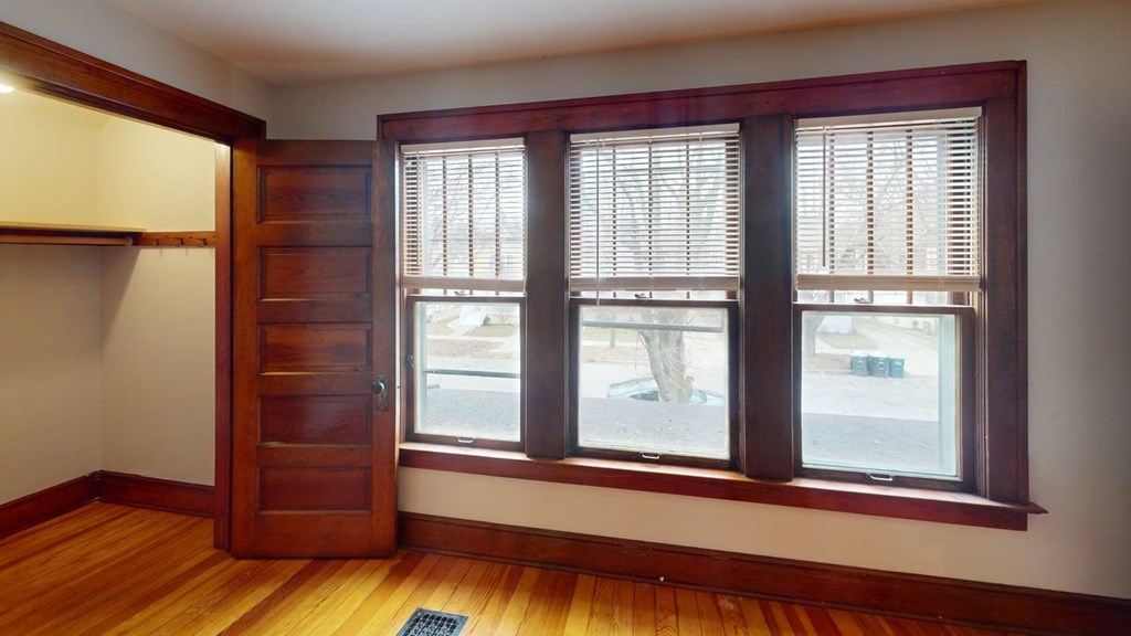A room with a wooden floor and a large window with blinds.