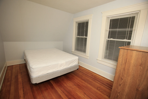 A white mattress is on a wooden floor in a room with a window.