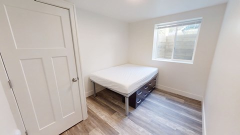 A small bedroom with a bed, dresser, and a door.