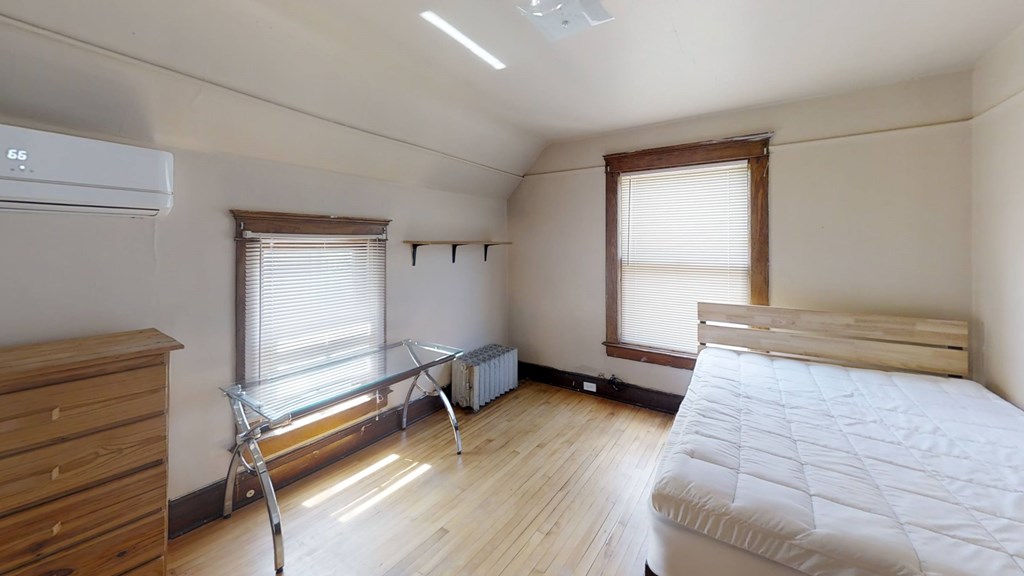 A bedroom with a bed, dresser, window, and air conditioner.