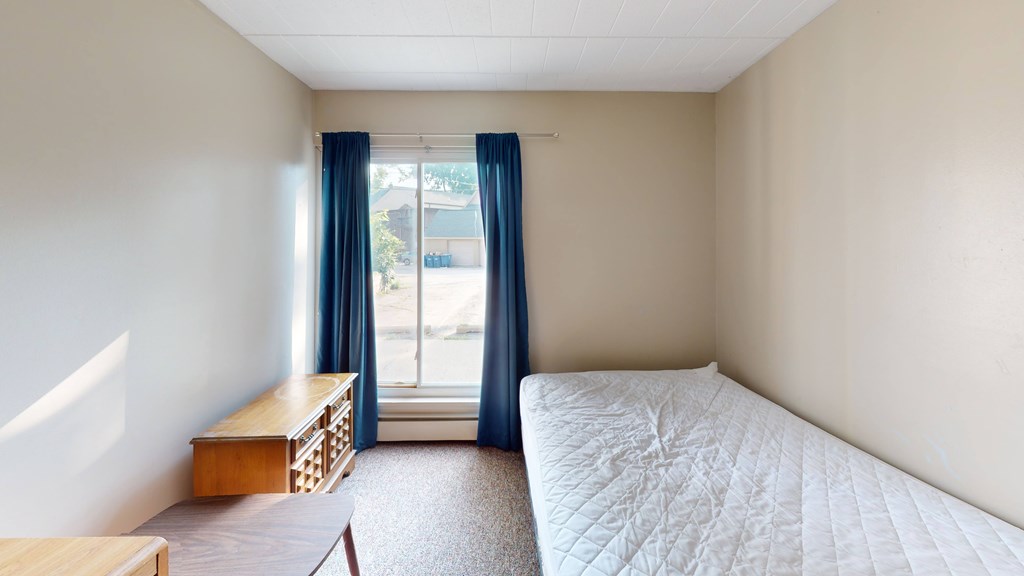 A bedroom with a bed, nightstand, and window with blue curtains.