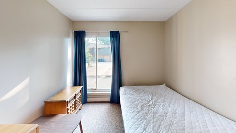 A bedroom with a bed, nightstand, and window with blue curtains.