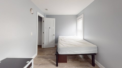 A bedroom with a bed, nightstand, and a window.