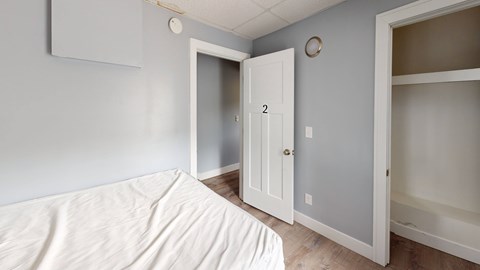 A white bed with a white sheet on it in a room with a white door and a white wall.