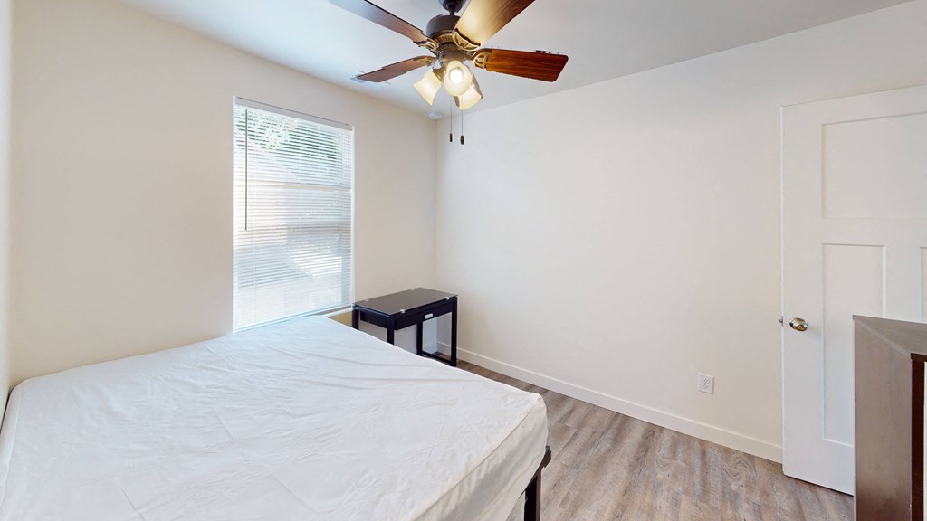 A bedroom with a bed, a ceiling fan, and a window.