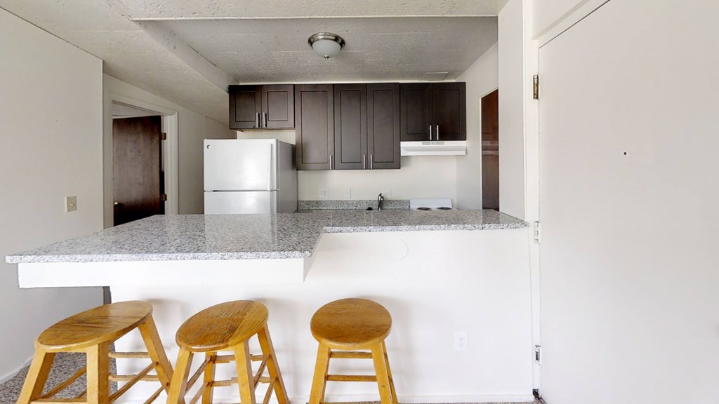 A kitchen with a white counter top and wooden bar stools.
