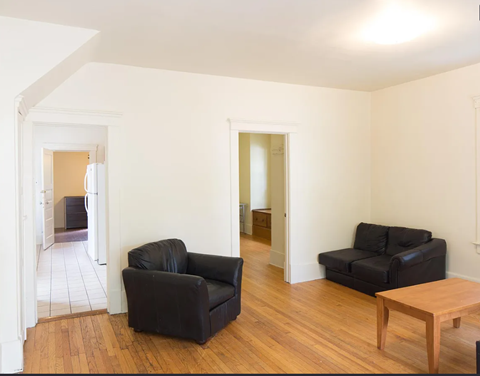 A black leather couch sits in a white room with wooden floors and white walls.