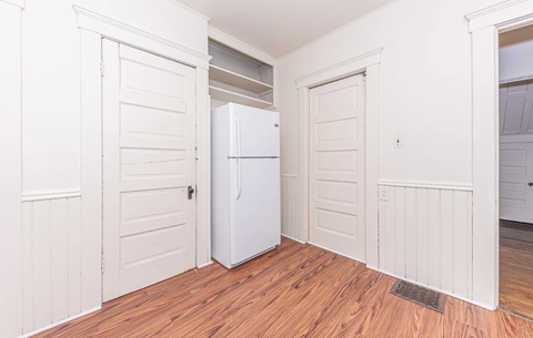 A white refrigerator is in a kitchen with white walls and wood floors.