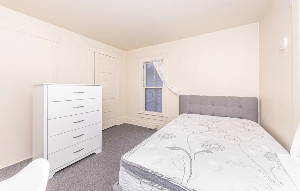 A bedroom with a bed, dresser, and window.