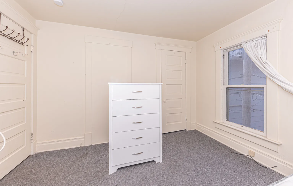 A white chest of drawers sits in a corner of a room with a window.