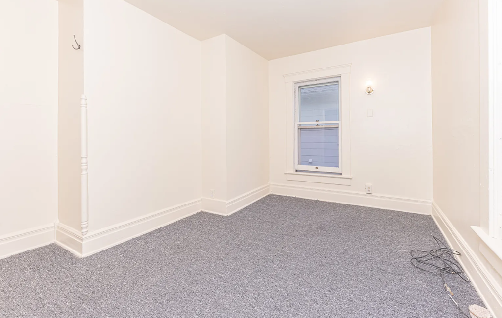 A room with a window and a grey carpet.