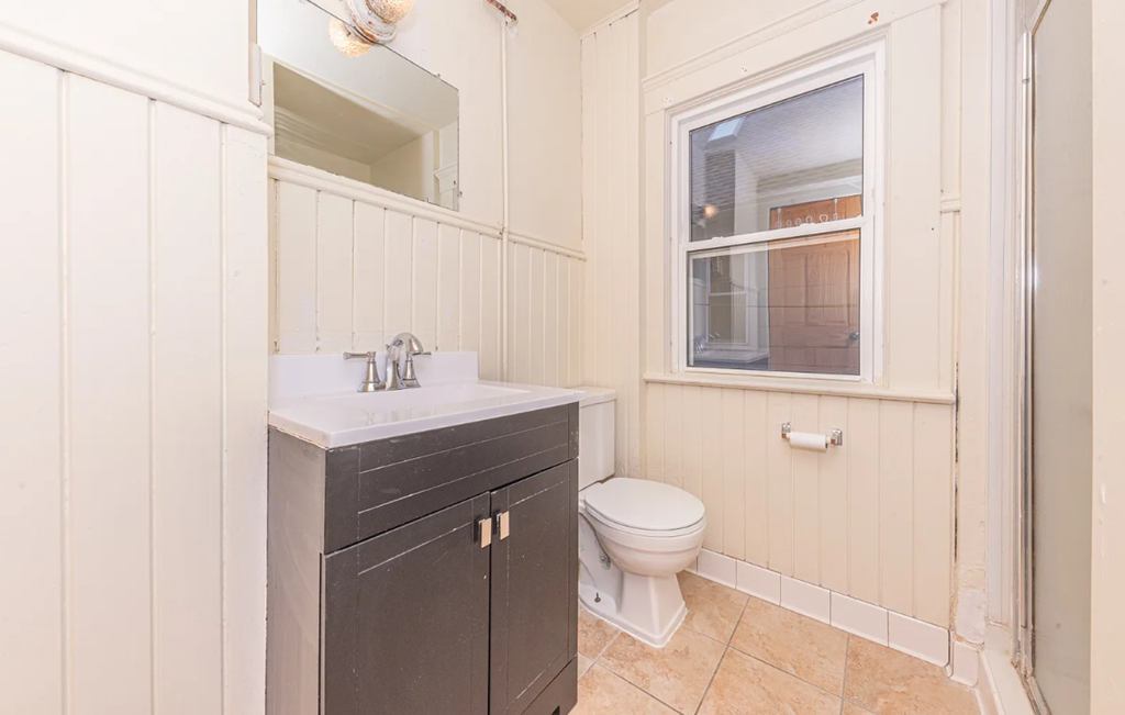 A bathroom with a toilet, sink, and a window.