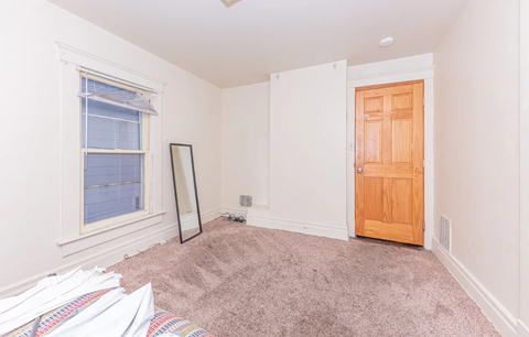 A room with a brown door, a window, and a mirror.