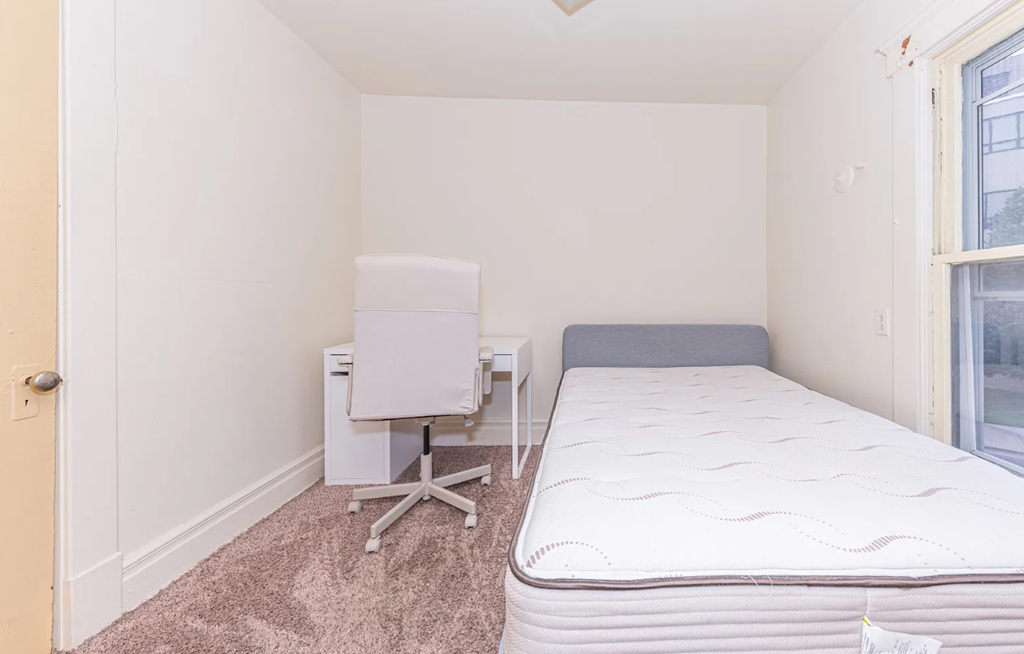 A white bed with a white chair and a white desk in a room.