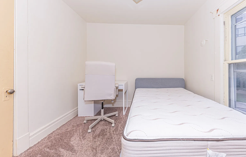 A white bed with a white chair and a white desk in a room.