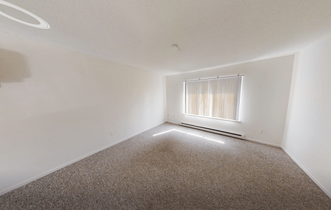 A room with a carpeted floor and a window with blinds.