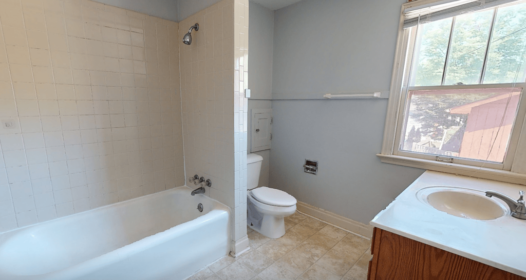 A white bathtub with a shower head and a white toilet in a bathroom.