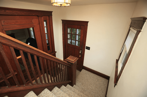 A wooden staircase with a carpeted runner and a chandelier hanging from the ceiling.