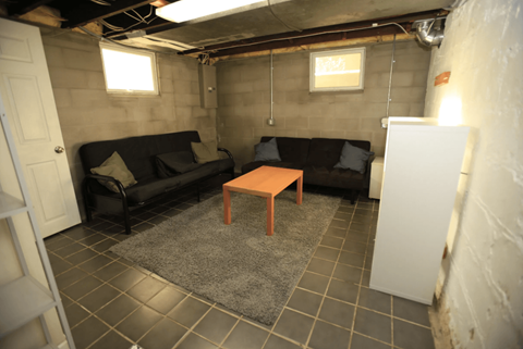 A room with a black couch, a wooden coffee table, and a grey rug.