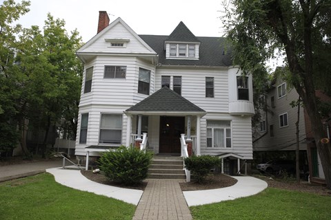 A white Victorian style house with a black roof and a brick walkway leading to the front door.