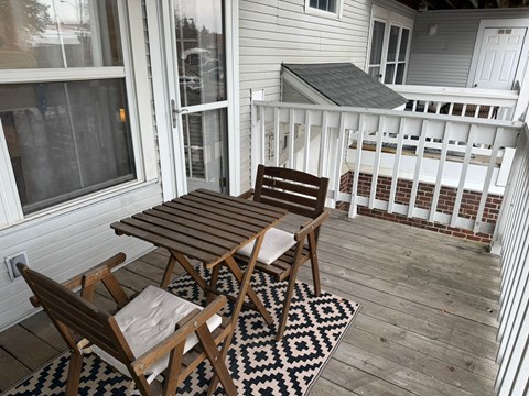 A wooden table and chairs are on a deck with a black and white patterned rug.
